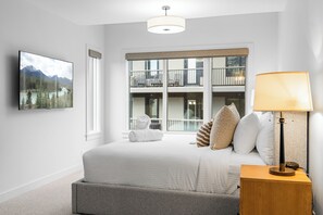 Habitación de hotel con cama, lámpara de noche, vista a un balcón con mobiliario exterior y un cuadro en la pared.