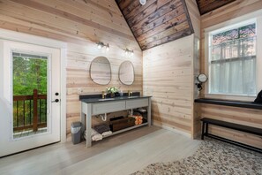 A bathroom with wooden walls, a vanity with a mirror, and a window with a view of trees. - Romantic Cabin Getaway Sauna, Hot tub & Pizza Oven (Broken Bow)