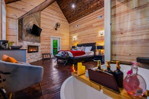Ein gemütliches Blockhaus-Interieur mit Kamin, einem Bett, einer Couch und einer Bar mit Flaschen.