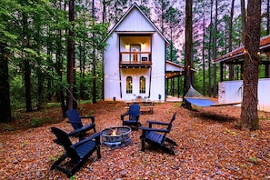 Une cabane avec un foyer extérieur, des sièges de jardin et un hamac.