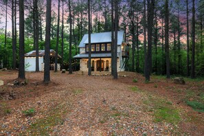 A two-story house with a stone facade and a metal roof, surrounded by a forest. - Romantic Cabin Getaway Sauna, Hot tub & Pizza Oven (Broken Bow)