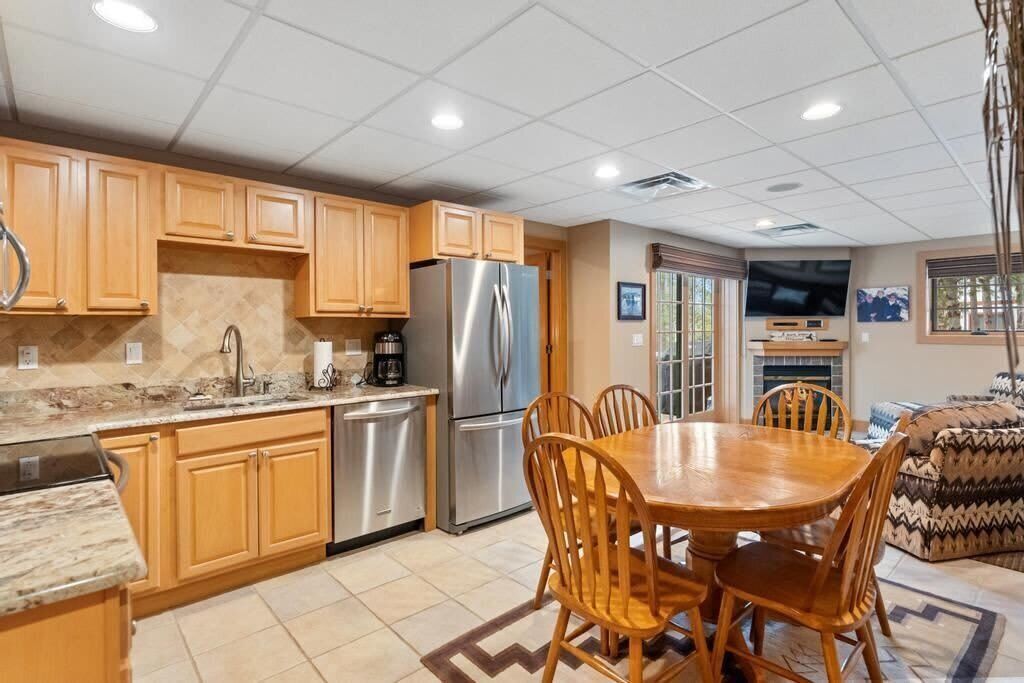 A kitchen with wooden cabinets, stainless steel appliances, a dining table with chairs, and a television mounted on the wall.