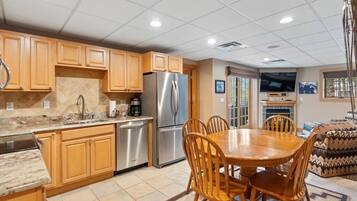 A kitchen with wooden cabinets, stainless steel appliances, a dining table with chairs, and a television mounted on the wall.
