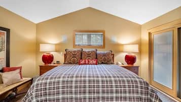 A bedroom with a large bed, two bedside lamps, a window with blinds, and a decorative pillow with the text 'Let It Snow'.