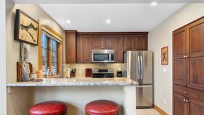A kitchen with wooden cabinets, stainless steel appliances, a marble countertop, and two red stools.