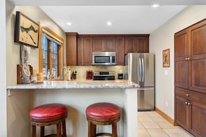 A kitchen with wooden cabinets, stainless steel appliances, a marble countertop, and two red stools.