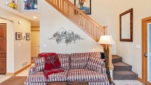 A living room with a sofa, a wooden staircase, a wall-mounted lamp, and a framed picture.