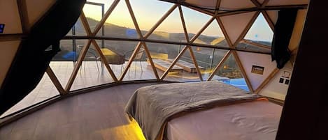 A room with a bed, a television mounted on the wall, and a view of the landscape.