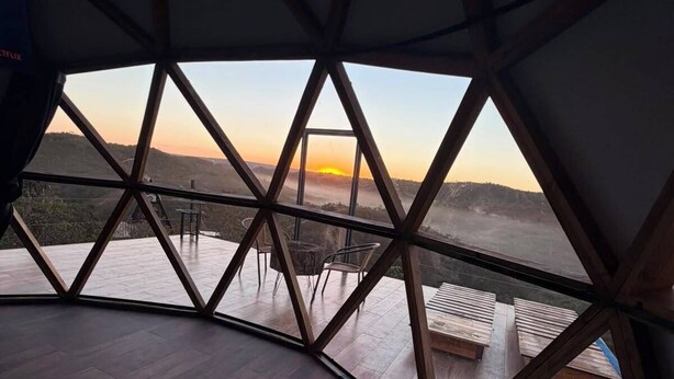 Una habitación con piscina de fondo de vidrio, suelo de madera y vistas a un paisaje ondulado al atardecer.