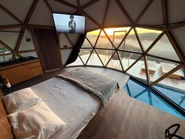 Un dormitorio con cama, televisor montado en la pared y vista a una piscina y paisaje.