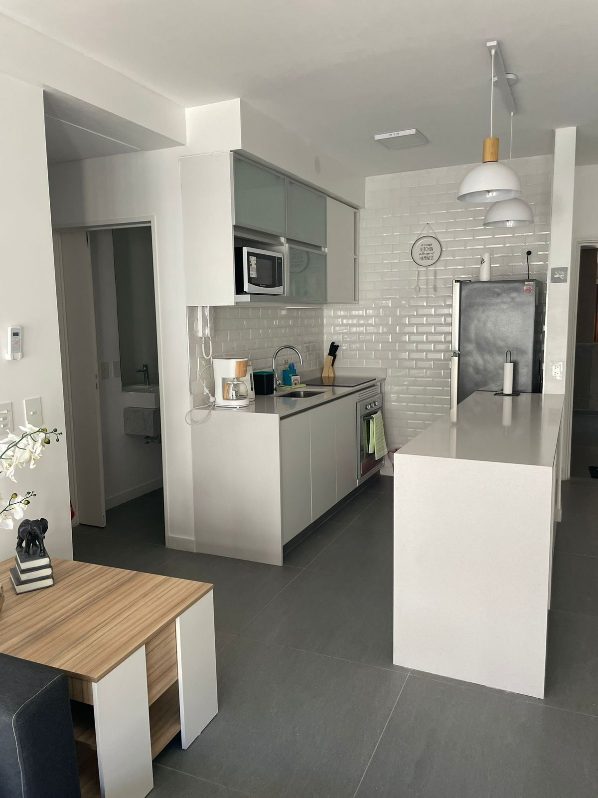 Una cocina moderna con armarios blancos, microondas integrado y refrigerador de acero inoxidable.