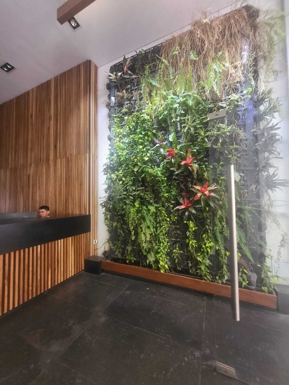 Zona de recepción con pared de jardín vertical, mostrador de madera y suelo de baldosas negras.
