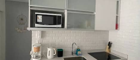 A compact kitchen with a microwave, coffee maker, sink, and a small oven.