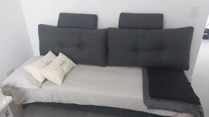 Una cama con cabecera gris, ropa de cama blanca y dos almohadones decorativos.