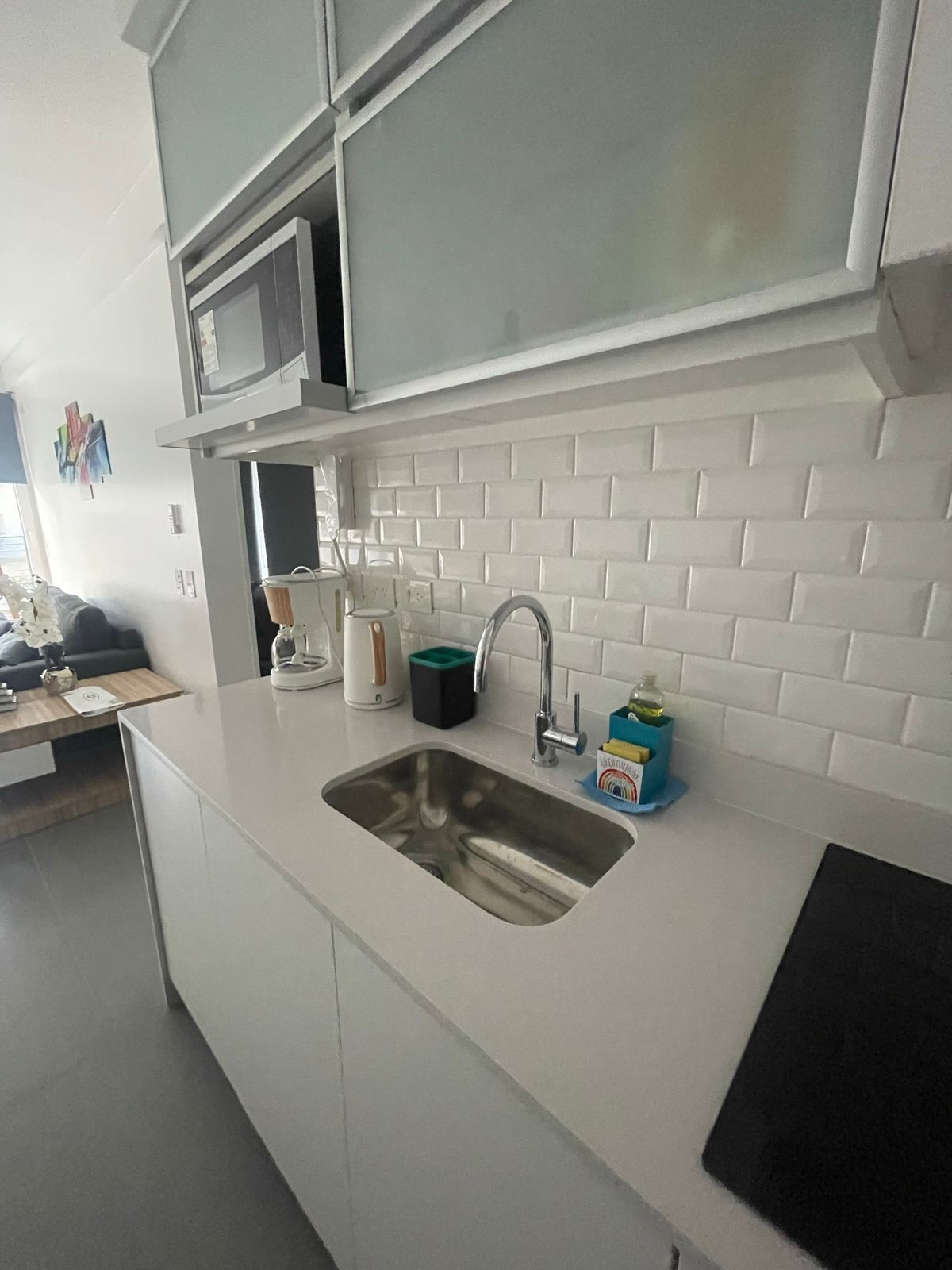 Et moderne køkken med en hvid bordplade, stålvask og en mikrobølgeovn over bordet.