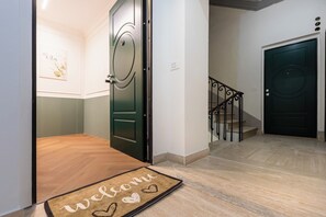 Ein Flur mit Holzboden, einer schwarzen Tür und einer Treppe mit Metallgeländer.