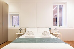 Una habitación de hotel con una cama grande, dos mesitas de noche con lámparas, una ventana con vistas a un edificio y un armario.