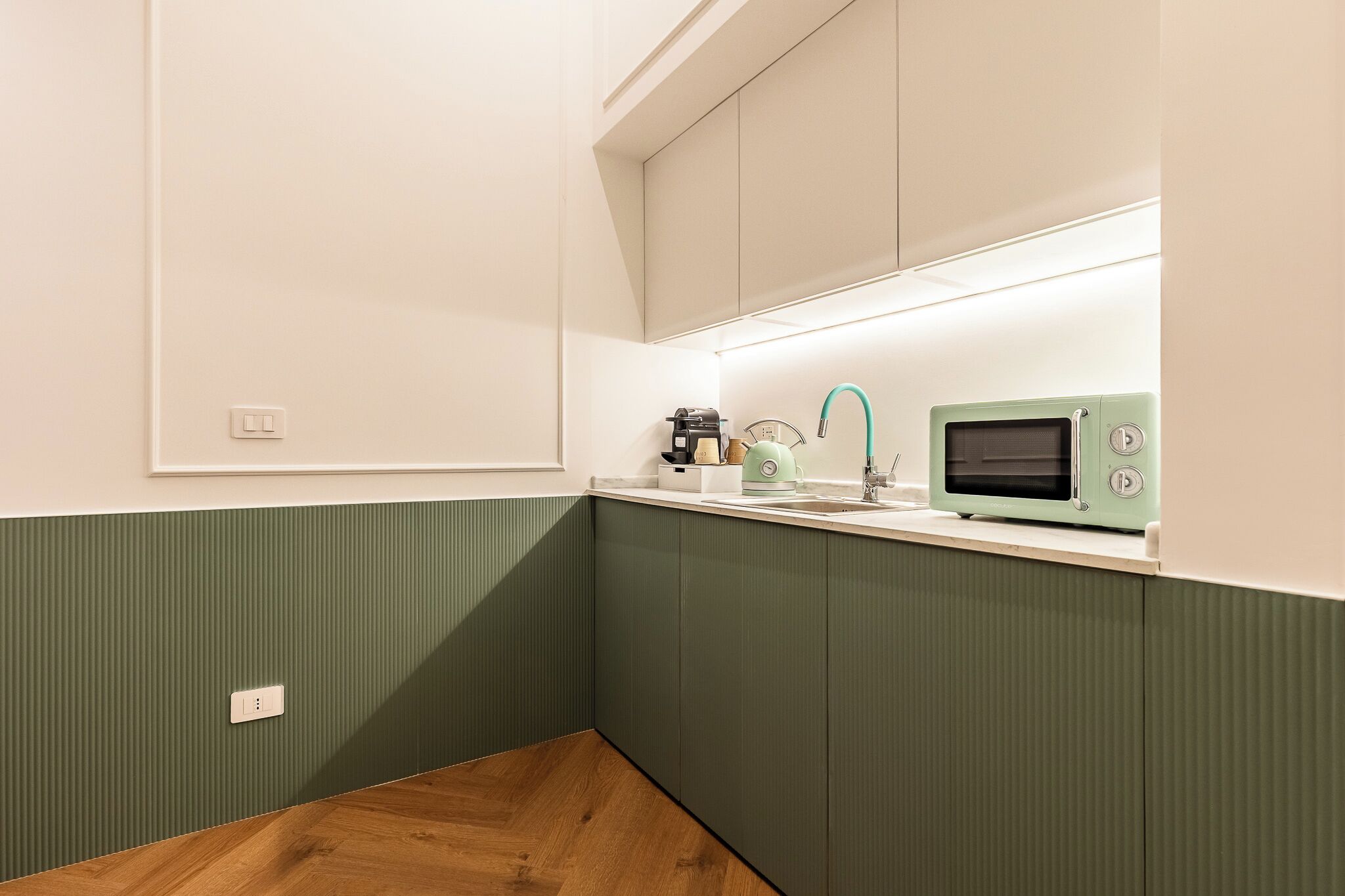 Una cocina con microondas incorporado, hervidor de agua y cafetera sobre la encimera.