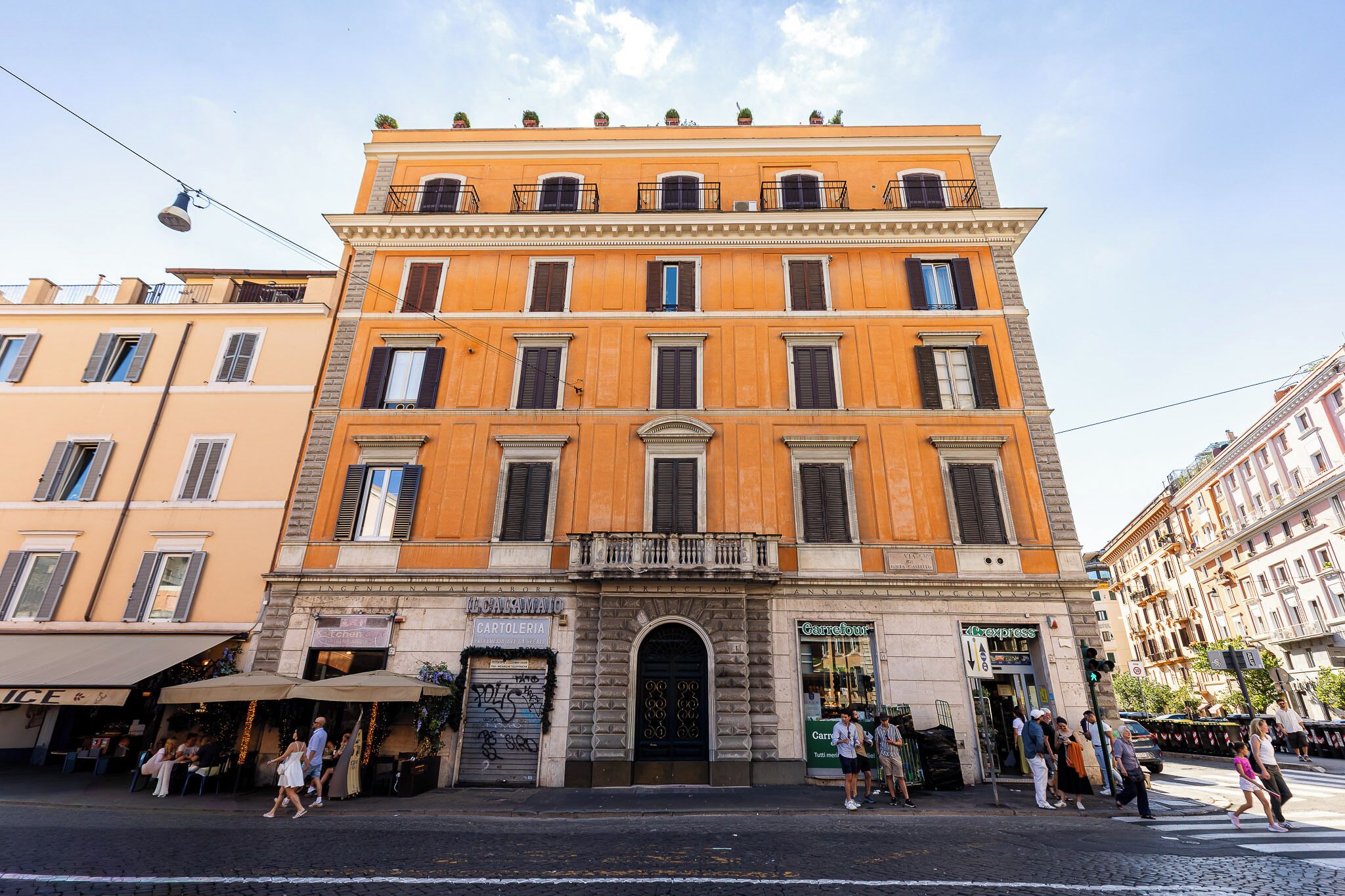 A multi-story building with a central entrance, storefronts on the ground floor, and a street in front.