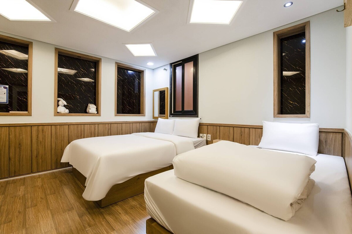 Quarto de hotel com duas camas, cabeceiras de madeira, piso de madeira e uma janela grande com vista.