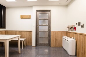 A room with a wooden table, a bench, a door with frosted glass panels, a wall-mounted heater, and a wall-mounted thermostat. - Yeongdeungpo Komodo Hotel (Seoul)