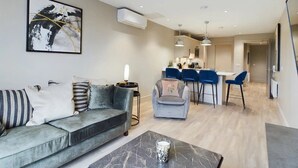 Un salon moderne avec un canapé gris, une table basse et un coin repas avec des chaises bleues.