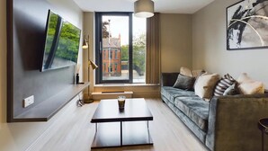 Un salon moderne comprenant un canapé, une table basse, un téléviseur fixé au mur et une grande fenêtre donnant sur des immeubles.