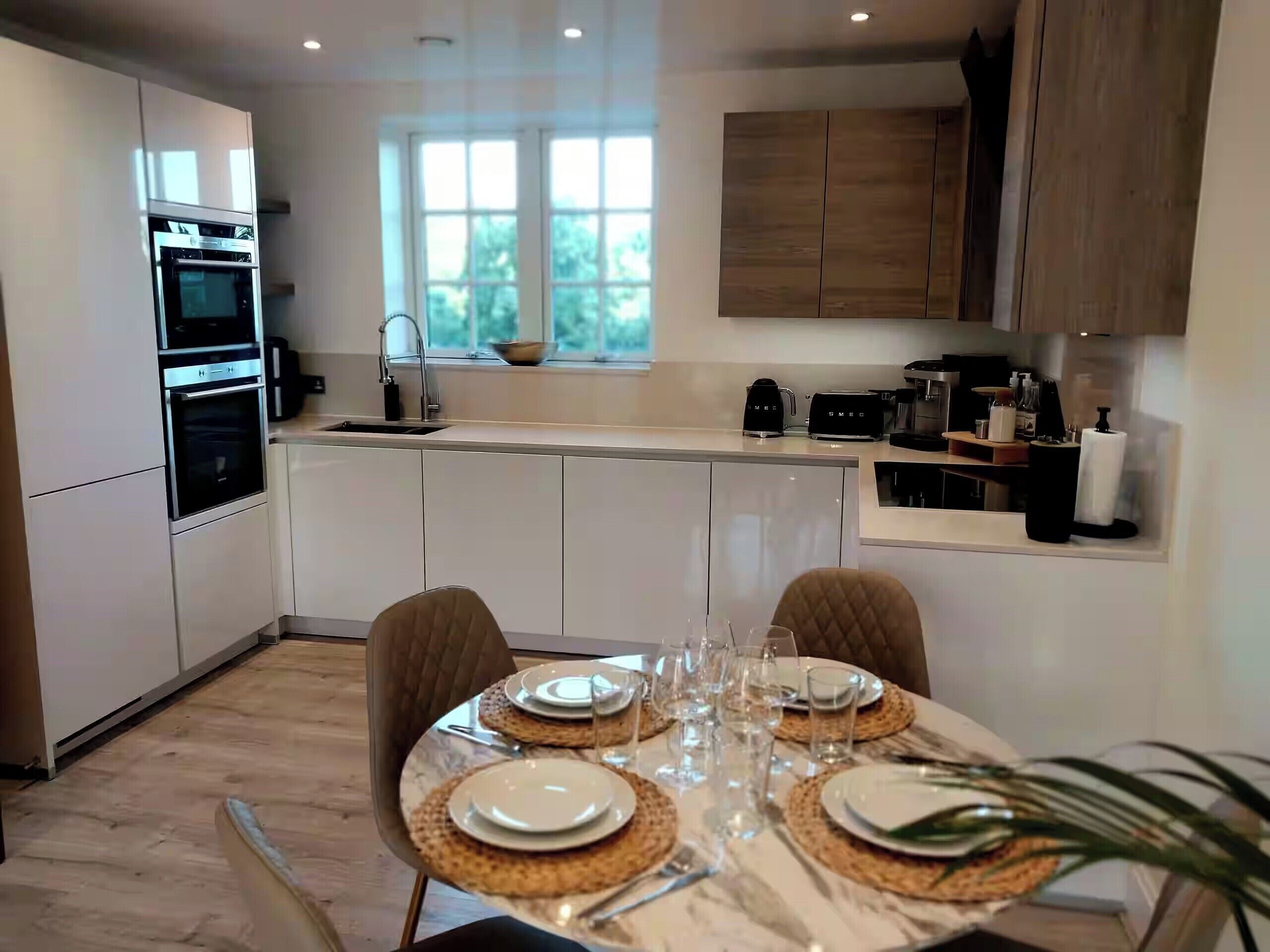 Una cocina moderna con electrodomésticos integrados, una zona de comedor con una mesa dispuesta para cuatro personas y un ventanal que proporciona luz natural.