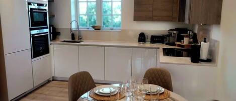 A modern kitchen with built-in appliances, a dining area with a table set for four, and a window providing natural light.