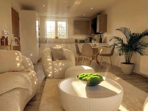 Ein modernes Wohnzimmer mit Sofa, Couchtisch mit einer Schüssel grüner Äpfel und einem Essbereich mit Stühlen und Tisch.