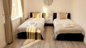 Ett hotellrum med två sängar, ett nattduksbord, en lampa och ett fönster med gardiner.