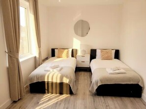 Ein Hotelzimmer mit zwei Betten, einem Nachttisch, einer Lampe und einem fenster mit Vorhängen.