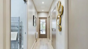 Um corredor com uma porta de vidro que dá para um banheiro, um radiador e uma porta com puxador dourado.