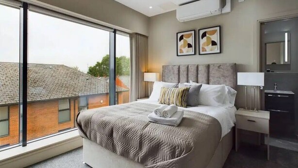 Quarto de hotel com cama grande, mesa de cabeceira, escrivaninha e vista para a cidade.