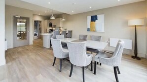 Uma sala de jantar moderna com uma mesa retangular e seis cadeiras, e uma cozinha ao fundo, além de um abajur.