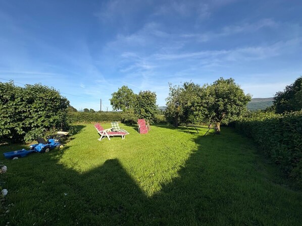 A grassy outdoor area with a lawnmower, two lawn chairs, and a small table.