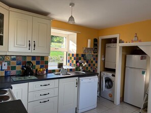 A kitchen with white cabinets, a tiled backsplash, a kettle, a sink, a washing machine, and a refrigerator.