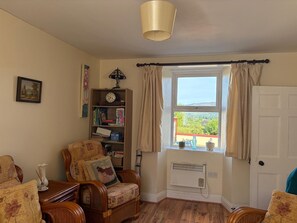 A room with a wooden chair, a bookshelf, a window with curtains, and a radiator.