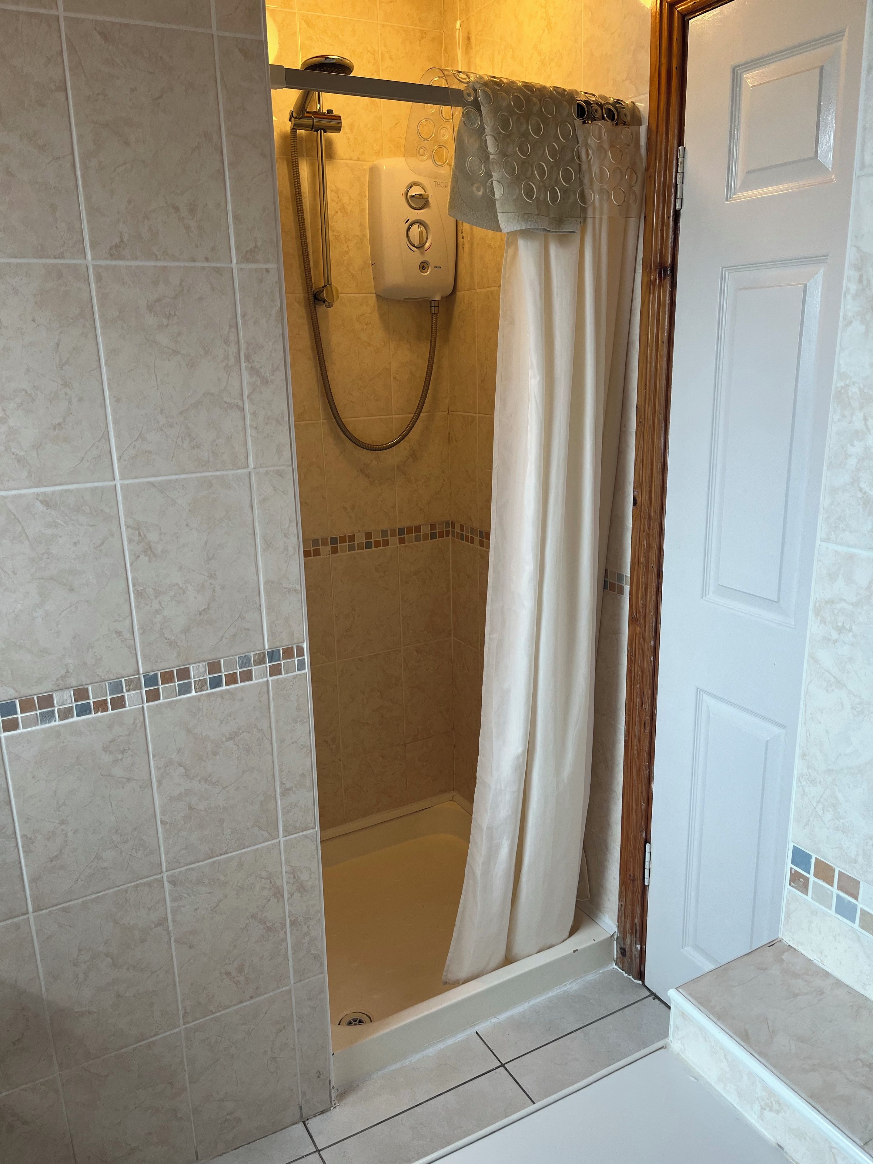 Un espace douche équipé d’un pommeau de douche à main, d’un panneau de commande et d’un rideau.