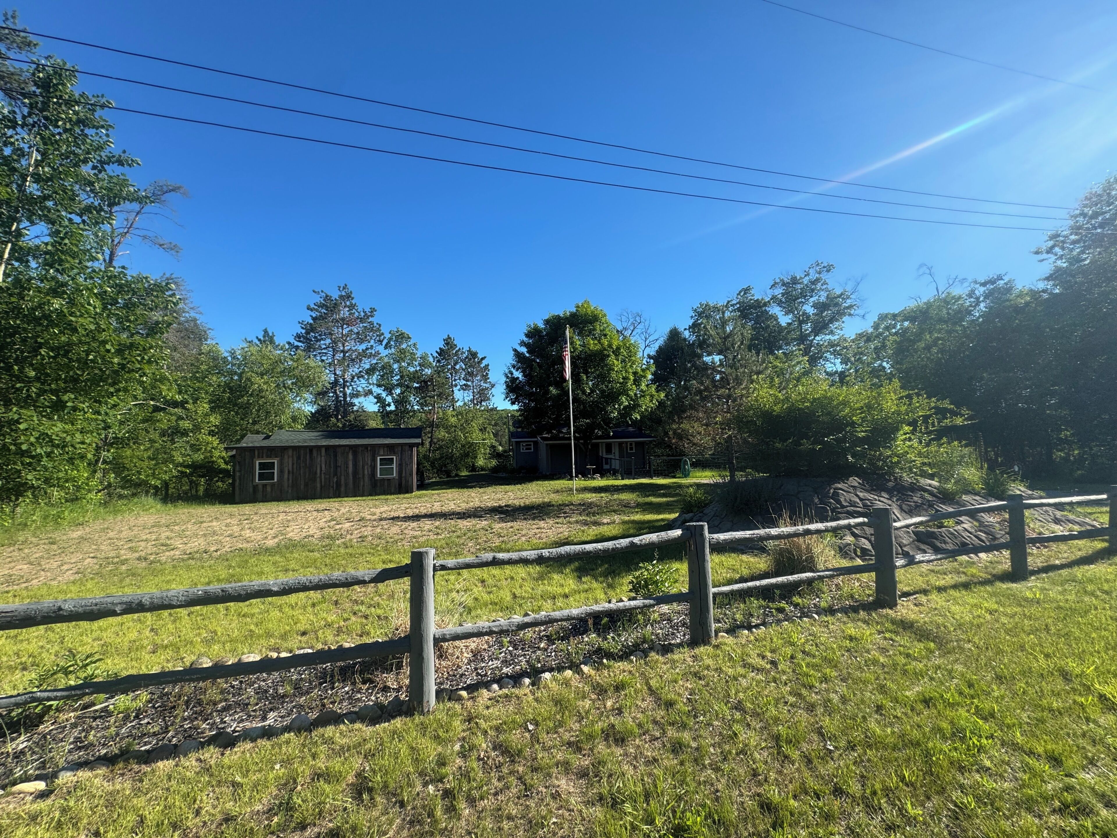 A fenced property with a small wooden building, a flagpole, and a grassy area.