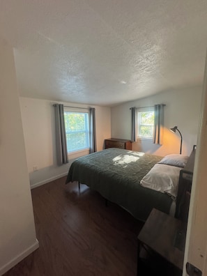 A bedroom with a bed, two bedside tables, a nightstand, a lamp, and a window with curtains.