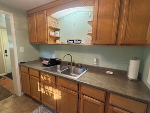 A kitchen with wooden cabinets, a double sink, and a shelf with a sign reading 'Sleepy Hollow'.