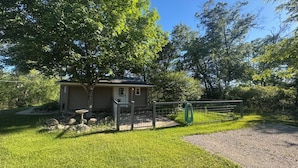 A small house with a front porch, surrounded by a fenced yard and trees. - Ride, Relax & Recharge at Sleepy Hollow Hideaway (Roscommon)