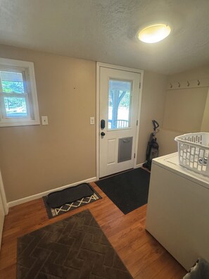 A laundry area with a washing machine, a door with a window, and a doormat.
