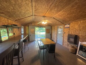 A rustic interior with a wooden ceiling, a bar area, a dining table with chairs, and a gas stove.