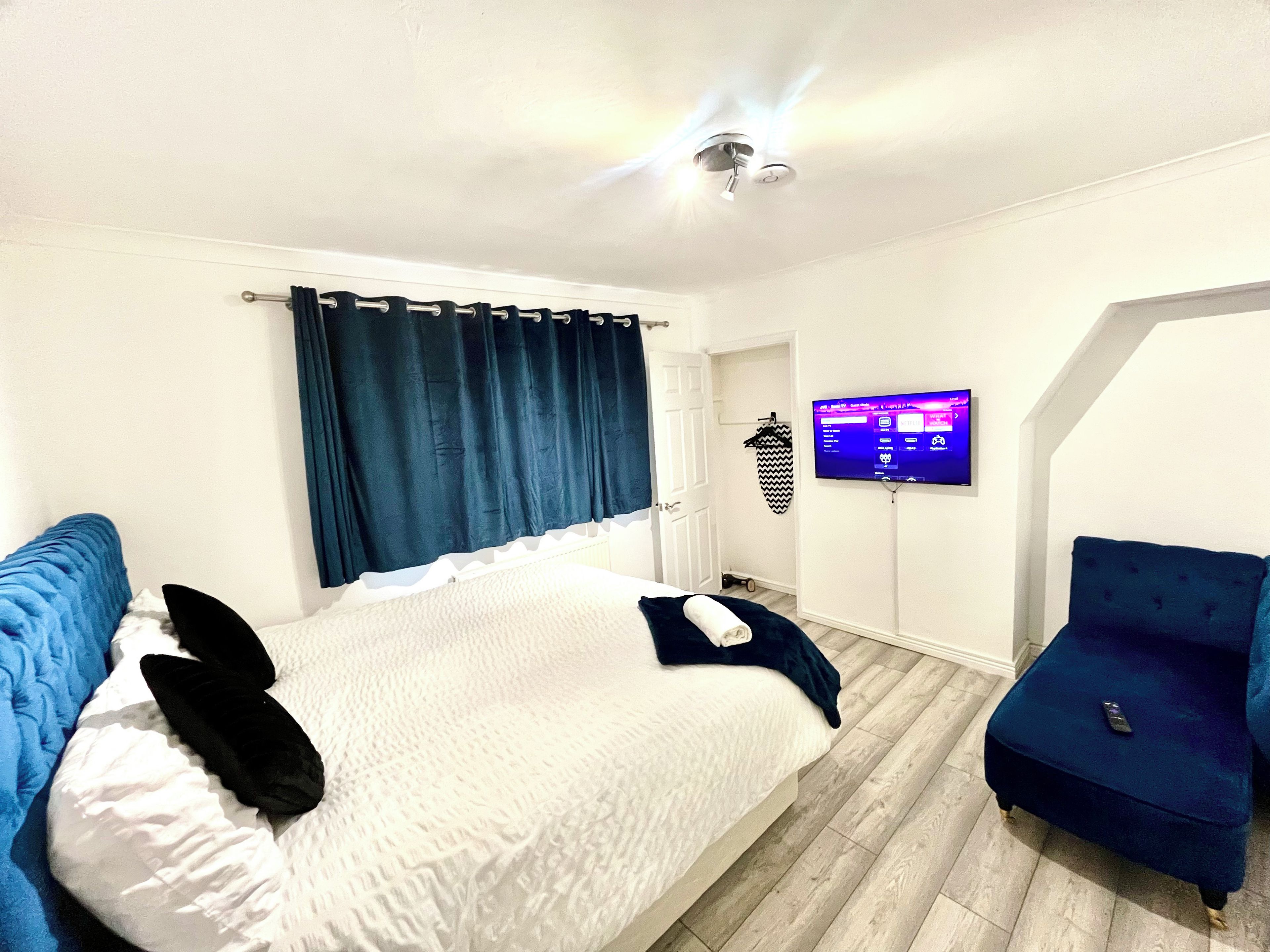A bedroom with a bed, a blue chair, a television, and a ceiling fan.