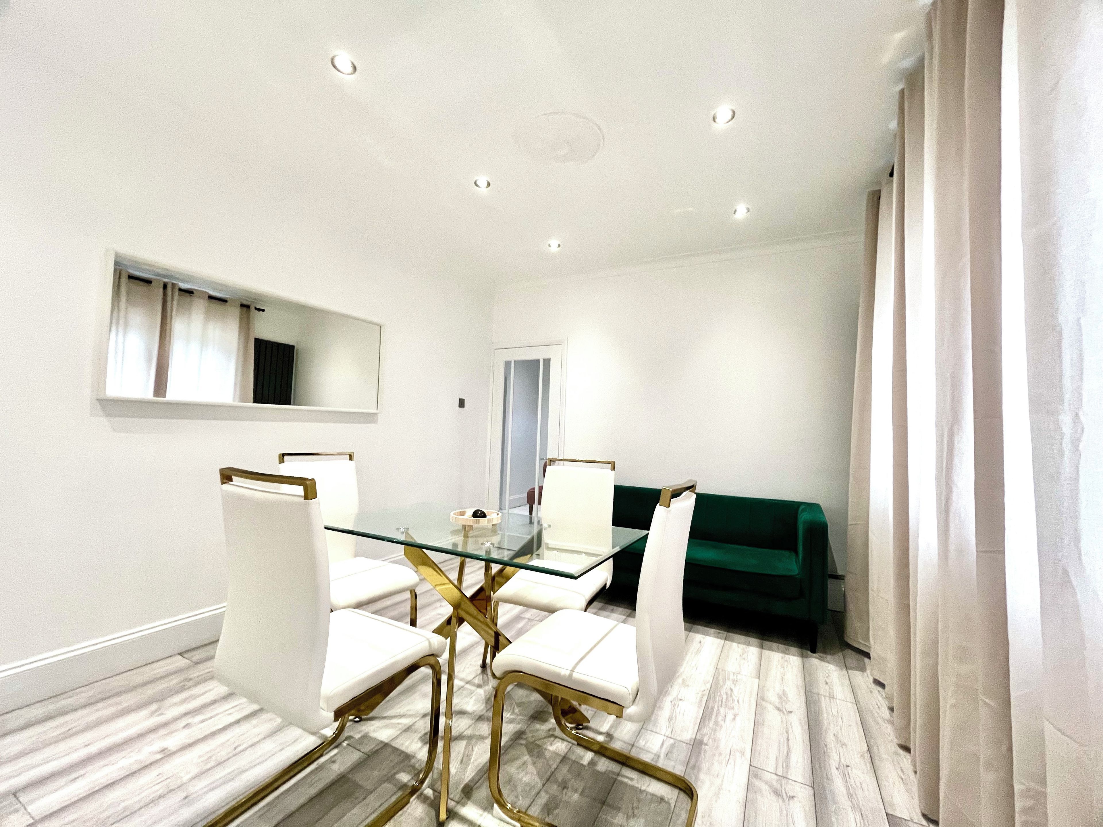 A modern dining area with a glass table, white chairs, and a green sofa.
