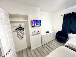 Ein Schlafzimmer mit einem Bett, einem Sessel, einem Fernseher an der Wand, einem Kleiderschrank und einer Tür.