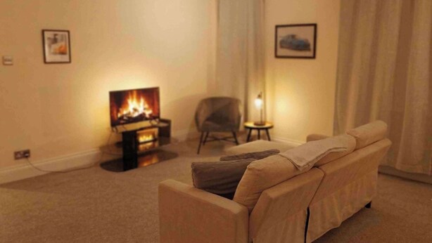 A living room with a sofa, a small table, a chair, a fireplace, and two framed pictures on the wall. - 1BR Apartment in Chislehurst High Street Sleeps 3 (Chislehurst)