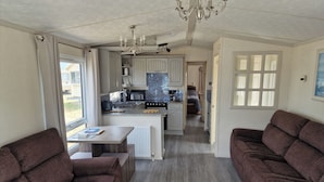 A modern kitchen with a central island, a dining area with a table and chairs, and a living area with sofas. - Caravan Sleeps 6 with Parking (Great Yarmouth)